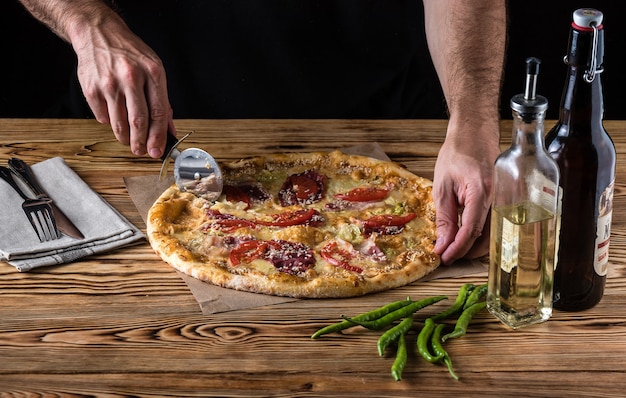 El chico corta pizza en una mesa de madera