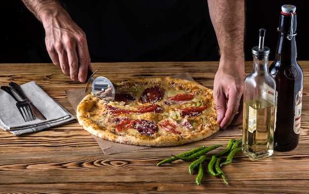 El chico corta pizza en una mesa de madera