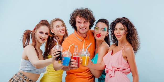 un chico y cuatro chicas con maquillaje colorido sosteniendo vasos de plástico y sonriendo