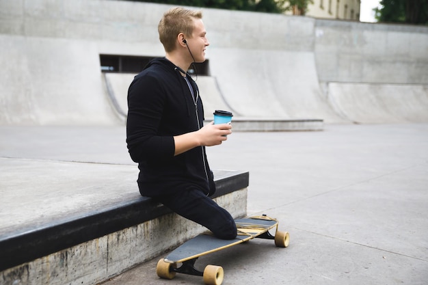 Chico discapacitado joven y motivado con una taza de café antes de montar en longboard en un skatepark