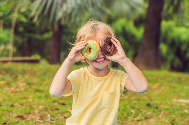 Chico divertido con donut. niño se divierte con donut. Comida sabrosa para niños. Tiempo feliz al aire libre con comida dulce.