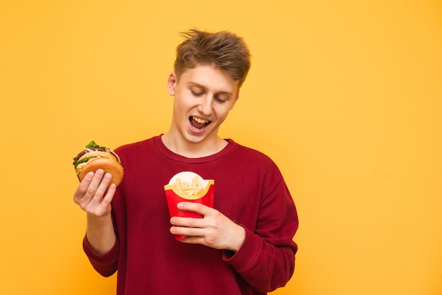 Chico divertido tiene papas fritas y una hamburguesa en el amarillo