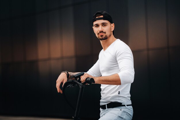 Chico elegante con una camiseta blanca y una gorra en un scooter eléctrico en la ciudad