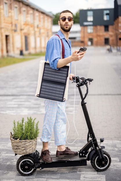 Chico elegante conduce scooter eléctrico y usa el teléfono en movimiento