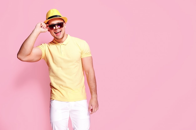 Chico elegante seguro en camisa amarilla, gafas de sol, pantalones cortos blancos, sombrero de paja