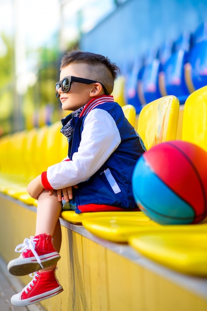 Chico elegante sentado en la cancha de baloncesto