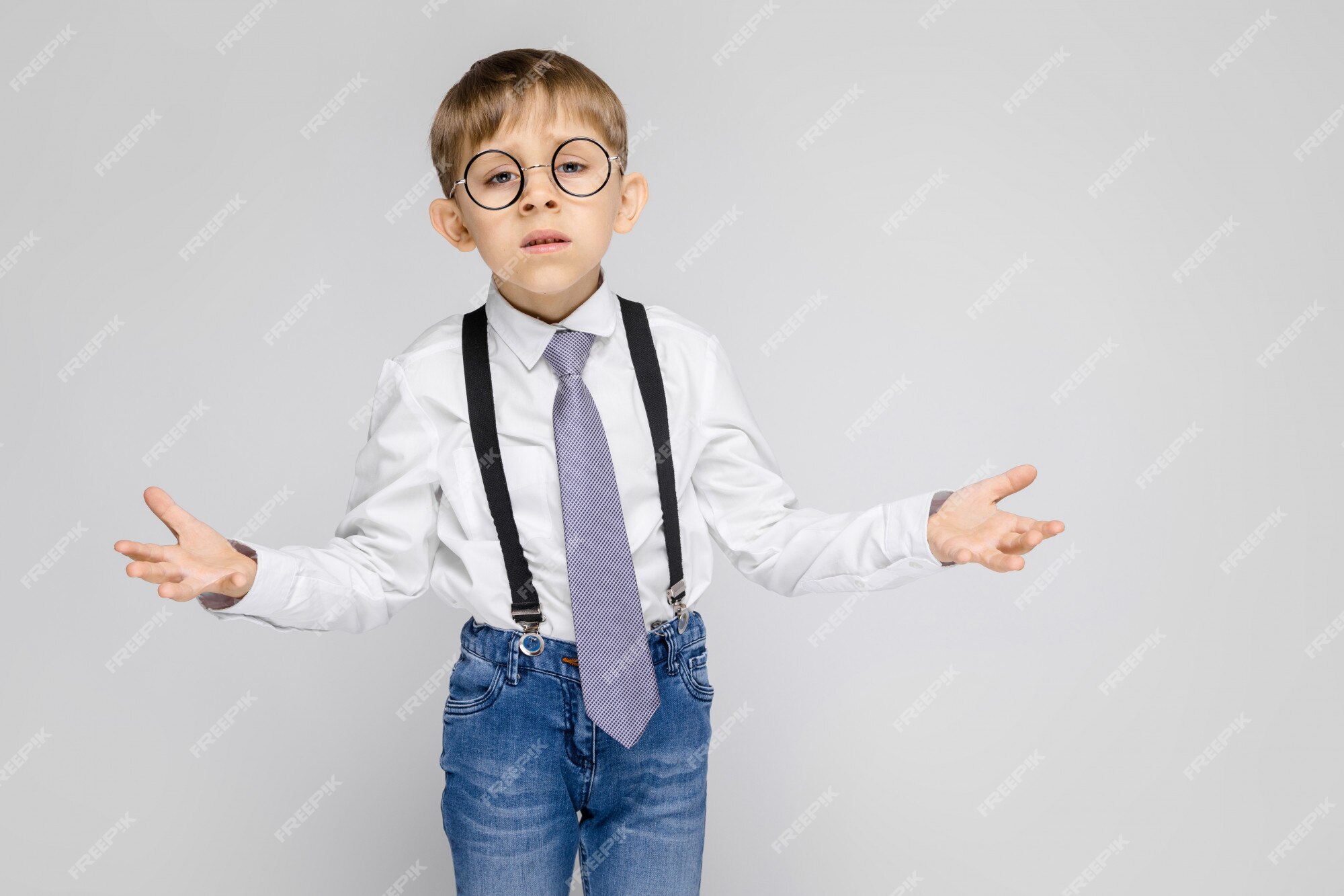 Un chico encantador con una camisa blanca, tirantes, una corbata y ligeros en gris Foto Premium