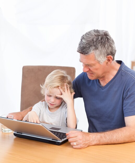 Chico encantador y su abuelo mirando su computadora portátil