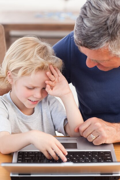 Chico encantador y su abuelo mirando su computadora portátil