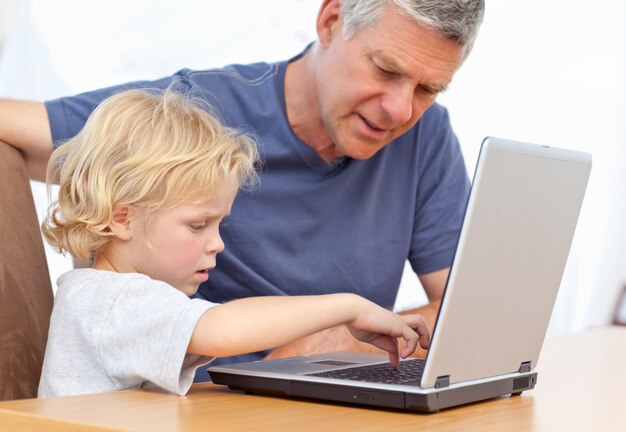 Chico encantador y su abuelo mirando su computadora portátil