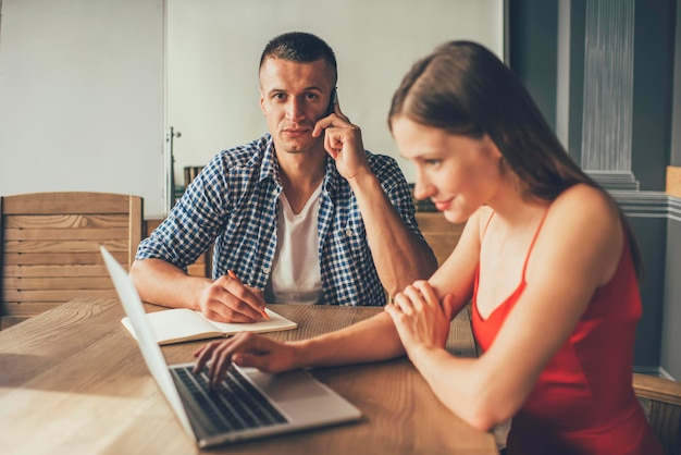 chico escribiendo notas hablando por teléfono trabajando con una encantadora mujer viendo una laptop sentada en la mesa