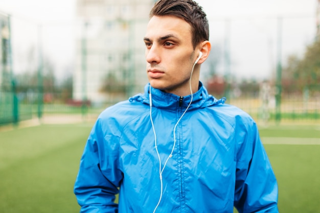 El chico escucha música durante un entrenamiento. Un joven practica deportes, corre en el campo de fútbol. El chico trabaja al aire libre y fresco.