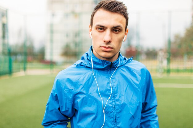 El chico escucha música durante un entrenamiento. Un joven practica deportes, corre en el campo de fútbol. El chico trabaja al aire libre y fresco.