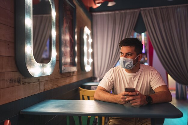 El chico español joven que lleva una mascarilla está sentado en un café; vida social durante la pandemia