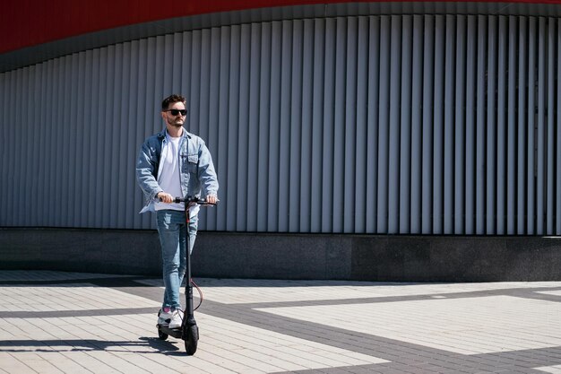 El chico está montando un scooter eléctrico contra el fondo de la ciudad. U cantar teléfono.