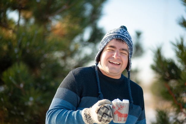 El chico está tomando una bebida caliente con malvaviscos en el invierno en el bosque.