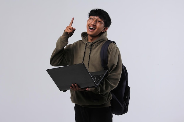 Chico estudiante asiático usando laptop y apuntando su dedo hacia arriba para expresar su idea