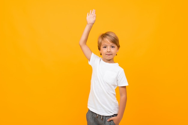 Chico europeo en una camiseta blanca con maqueta con una mano levantada sobre un fondo naranja con espacio de copia
