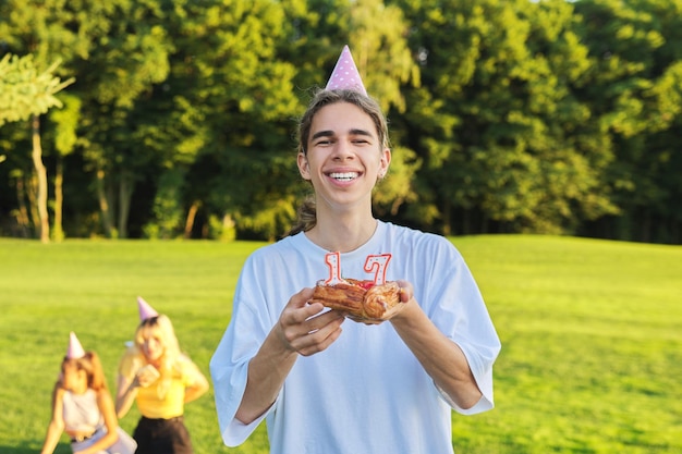 Chico feliz adolescente en sombrero de cumpleaños con pastel con velas 17