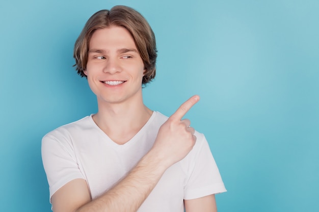 Chico feliz aislado mostrando promoción señalando con el dedo fondo azul espacio vacío