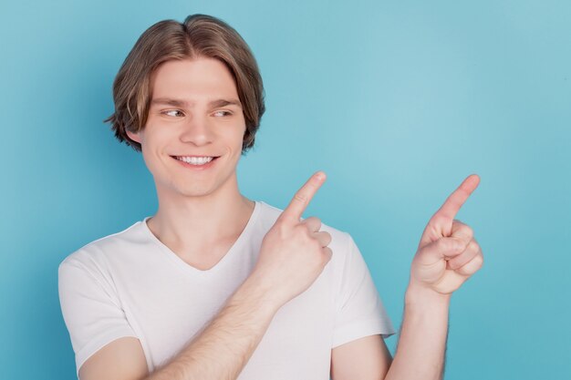 Chico feliz aislado mostrando señalando anuncios promocionales con fondo de espacio vacío azul de dedo