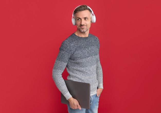 Chico feliz con auriculares para escuchar podcast de audio en el fondo rojo de la computadora portátil en línea