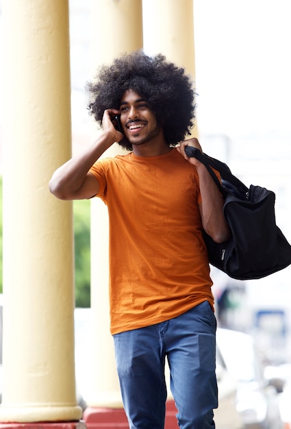 Chico feliz caminando en la ciudad con teléfono móvil y bolso