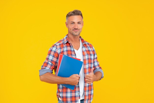 Chico feliz en casual dando pulgar sosteniendo libros escolares educación de fondo amarillo