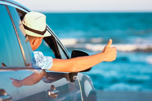 Un chico feliz en el coche junto al mar en la naturaleza en viajes de vacaciones