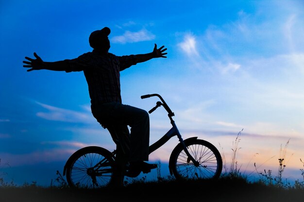 Un chico feliz en un concepto de bicicleta en el parque en la silueta de viaje por la naturaleza