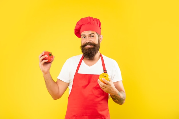 Chico feliz en delantal de cocina y toque con tomates rojos y amarillos cocinero de fondo amarillo