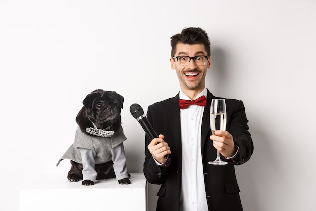 Chico feliz levantando copa de champán, dando micrófono al perro disfrazado