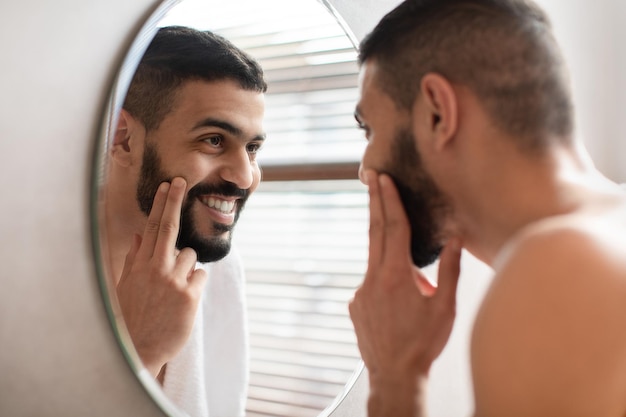 Chico feliz mirándose en el espejo aplicándose crema en la cara