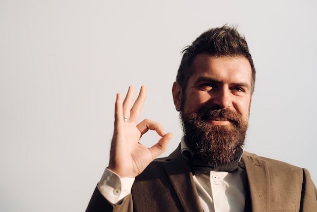 Chico feliz mostrar signo ok en cielo gris Sonrisa de hombre barbudo con gesto de mano al aire libre Empresario sonriendo con barba y bigote en la cara sin afeitar Acuerdo y espacio de copia de aprobación