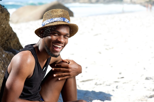 Chico feliz sentado en la playa con sombrero