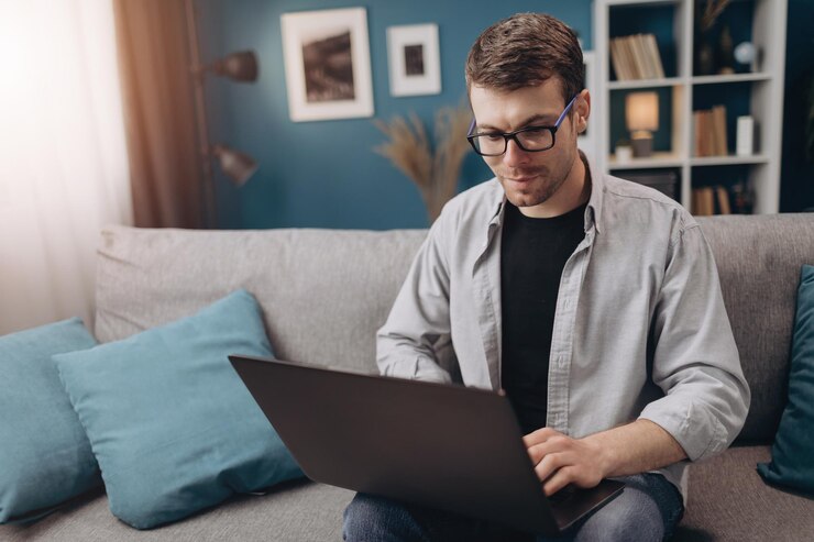 Chico feliz usando una computadora portátil mientras está sentado en un sofá gris
