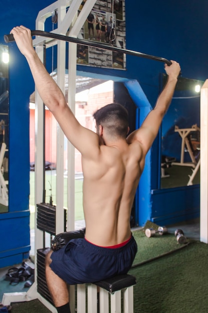 Chico fitness entrenando su espalda con una máquina en el gimnasio.