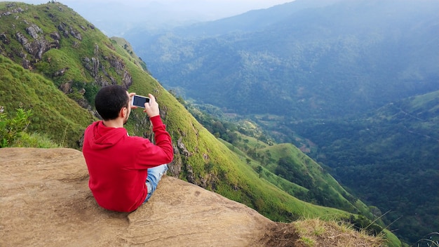 Foto un chico fotografía un paisaje de montaña sentado en el borde