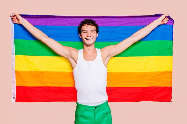 Chico gay alegre sosteniendo la bandera del arco iris en el estudio