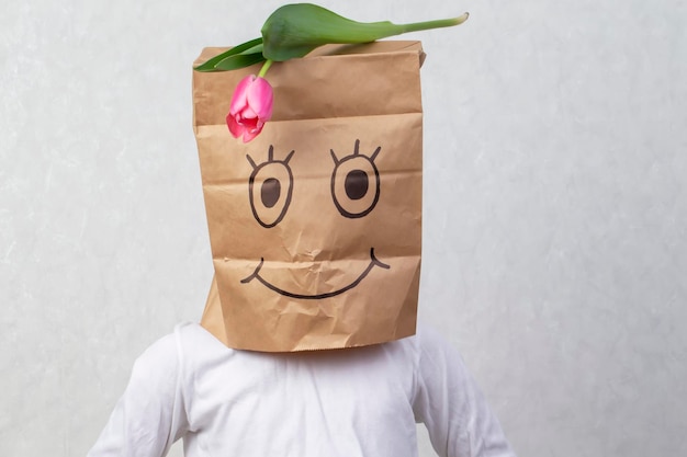 Un chico gracioso puso una bolsa de papel con una sonrisa pintada en su cabeza y puso un tulipán en él
