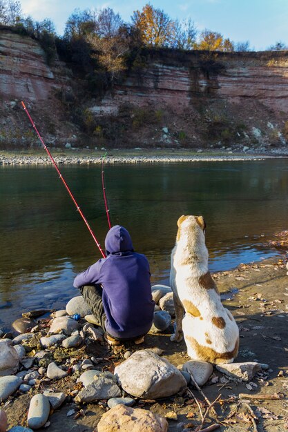 Un chico con un gran Pastor de Asia Central pescando en el río en un día de otoño