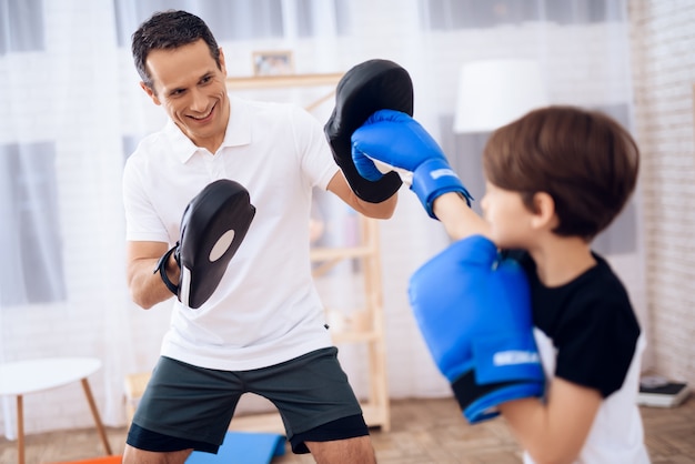 Chico en guantes de boxeo y entrenador de hombre en apartamento.