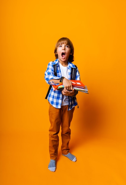 Chico guapo de 7 años con mochila sosteniendo libros sobre fondo amarillo para el concepto de educación