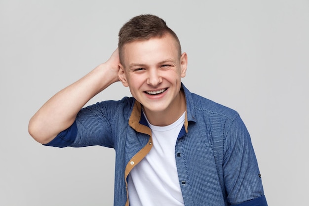 Chico guapo adolescente positivo mirando a la cámara con una sonrisa manteniendo la mano en la cabeza