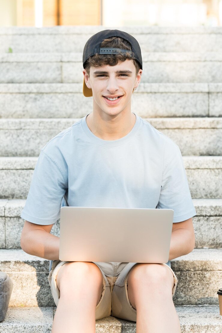 Chico guapo adolescente trabajando en la computadora portátil y sonriendo a la cámara