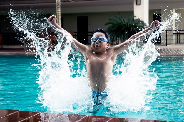 Chico guapo asiático saltando en la piscina