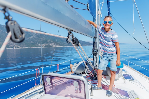 Chico guapo a bordo del velero en crucero de verano. Viaje de aventura, navegando con niños en vacaciones familiares. Ropa de niño en estilo marinero, moda náutica.