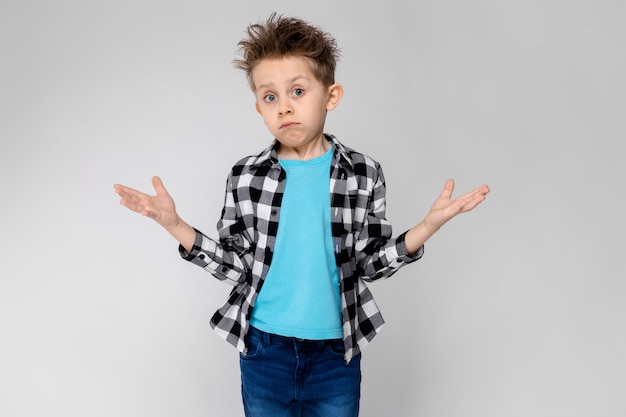 Un chico guapo en una camisa a cuadros, camisa azul y pantalones vaqueros se encuentra. El niño extendió las manos en ambas direcciones.