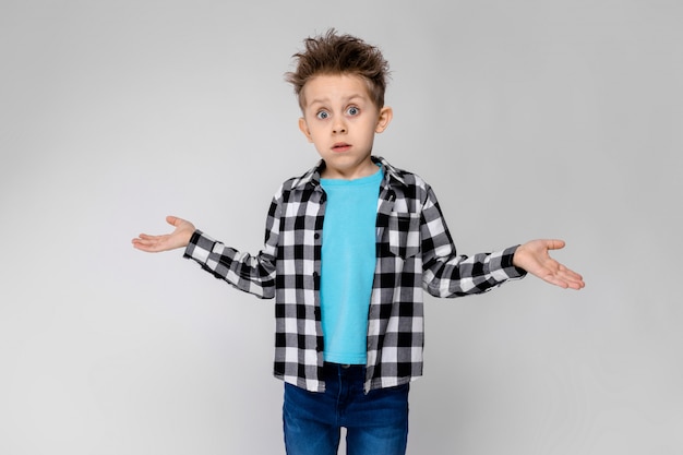 Foto un chico guapo en una camisa a cuadros, camisa azul y pantalones vaqueros se encuentra. el niño extendió las manos en ambas direcciones.