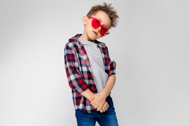 Un chico guapo en una camisa a cuadros, camisa gris y pantalones vaqueros se encuentra en gris